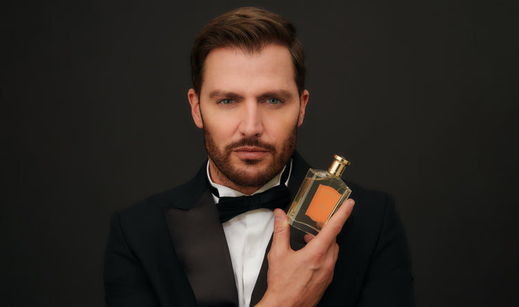 A man in a tuxedo holding a bottle of perfume against a dark background.