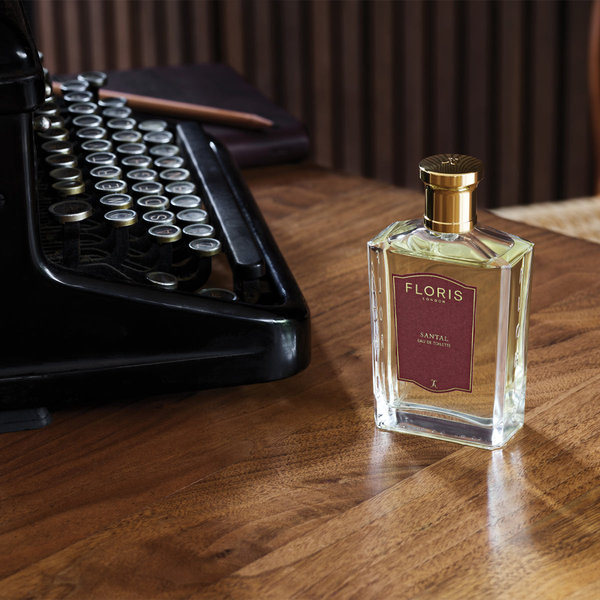 A "Santal - Eau de Toilette" by Floris London rests on a wooden table next to a vintage typewriter, showcasing its signature scent.