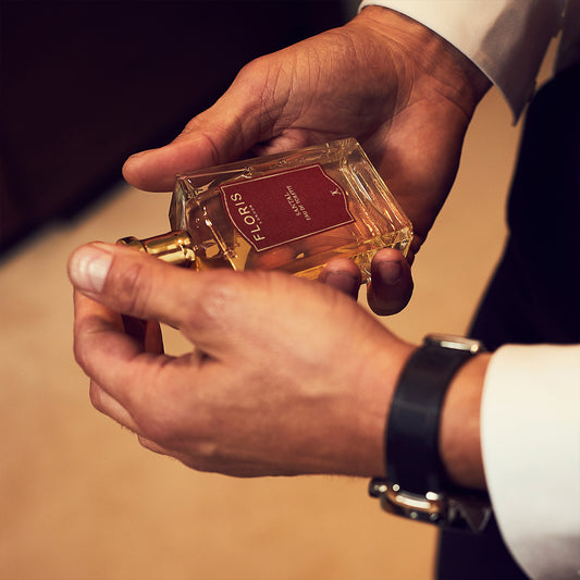 A man holds a Floris London Santal - Eau de Toilette bottle, dressed in a white shirt and watch—reflecting the essence of a men's signature scent.