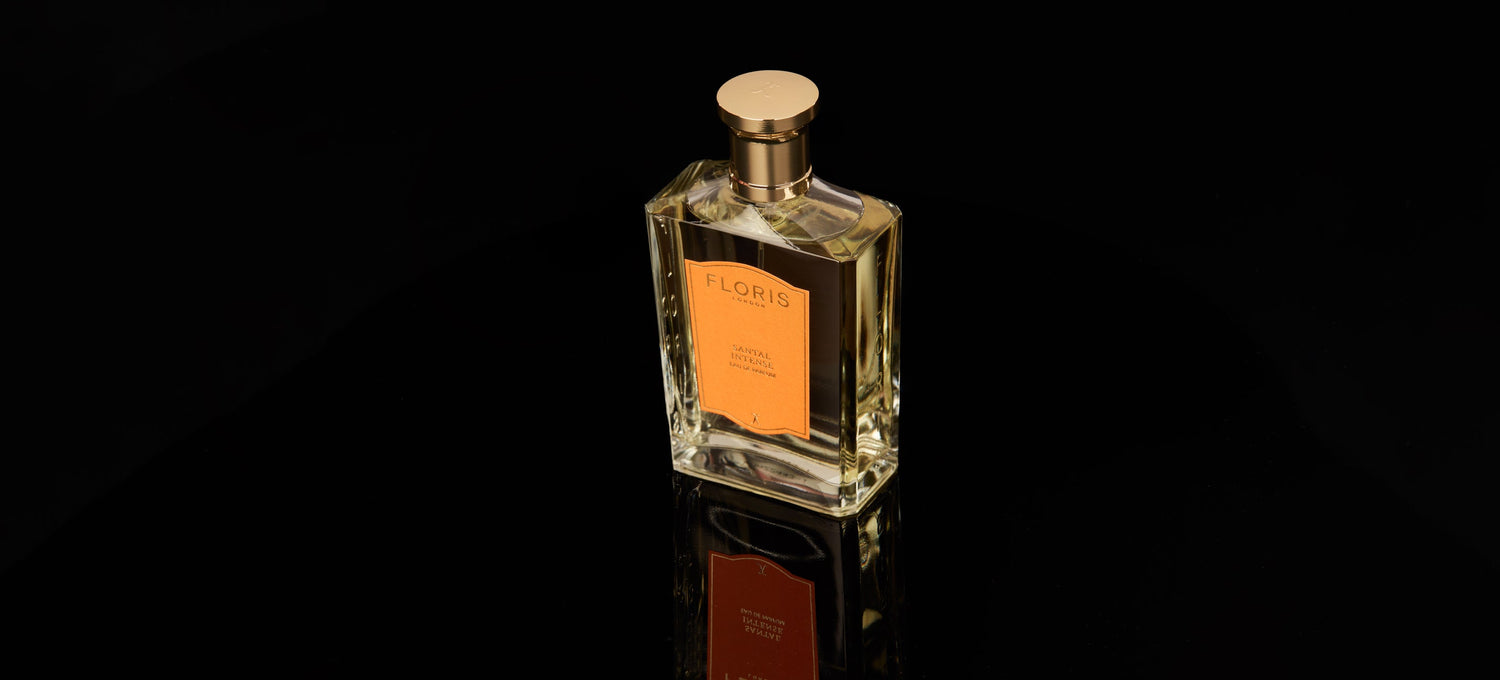 Clear glass bottle of Floris perfume with a gold cap, placed on a reflective black surface.