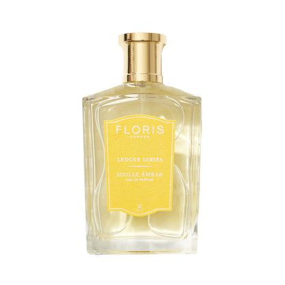 A clear glass perfume bottle with a gold cap labeled "Floris London UK Soulle Ámbar," infused with pineapple and amber notes.