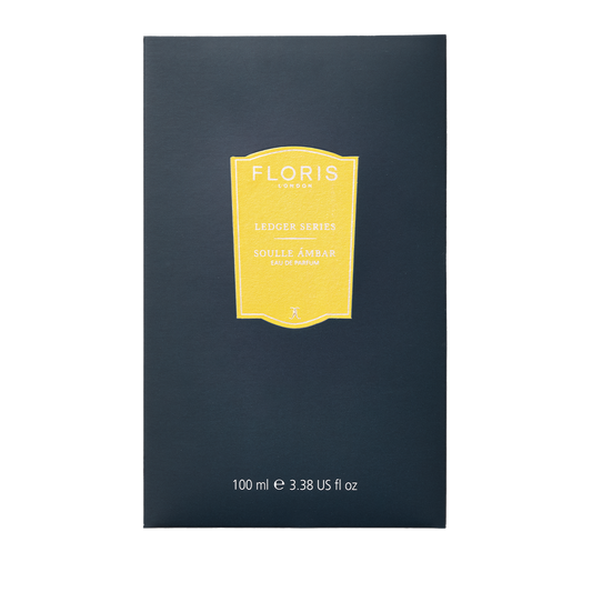 A dark blue box of Floris London Soulle Ámbar Eau de Parfum, 100ml, with a yellow label, features a warm amber and fruity pineapple scent.