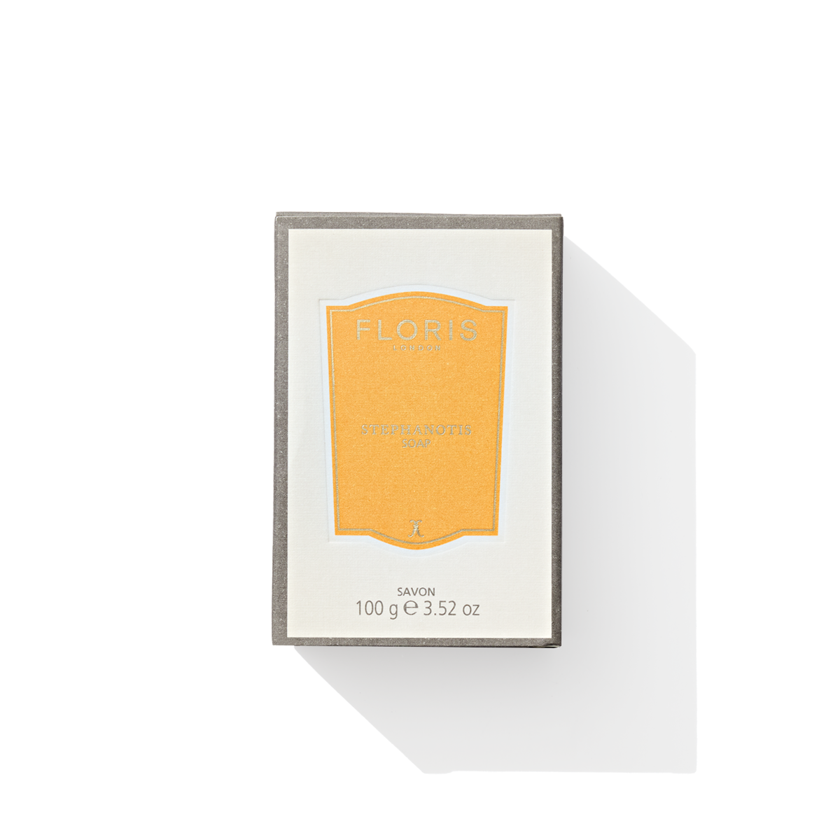 A rectangular box of Floris London Stephanotis - Luxury Soap with an orange label, casting a shadow, evokes the luxurious experience of fragranced soap inside. Its floral aroma transports you to a blooming garden, reminiscent of Stephanotis petals wafting through the air.