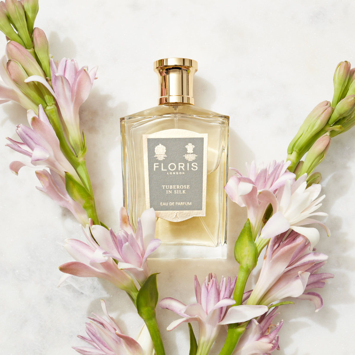 A bottle of "Tuberose in Silk - Eau de Parfum" by Floris London is set amidst pink and white tuberose and jasmine flowers on a white background.