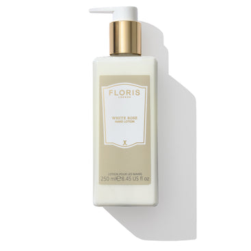 A bottle of Floris London White Rose - Hand Lotion, enriched with sweet almond oil and vitamin E, featuring a white pump and gold label, lays elegantly on a white surface.