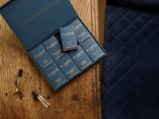 A Floris London Sample Set with fragrance vials is displayed on a wooden table next to a blue quilted surface.