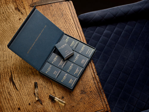 A Floris London UK Sample Set is open on a wooden table beside navy quilted fabric, displaying the brand’s signature fragrances.
