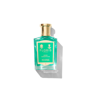 A bottle of Floris London Rose Geranium Bath Essence with a gold cap and green label, set against a white background.